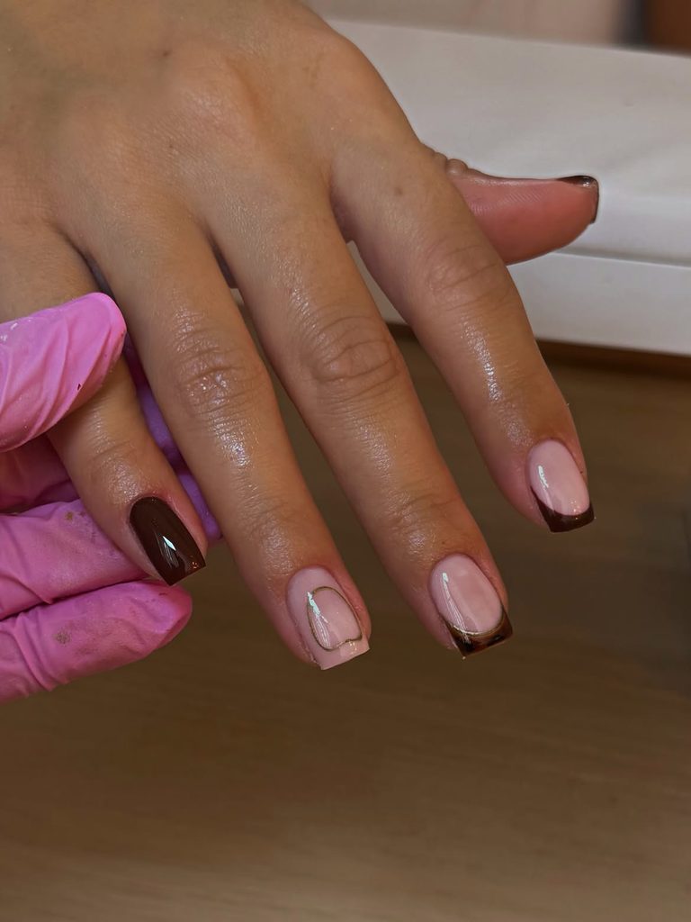 Short square nails with deep chocolate, sheer nude with gold line art, and chocolate French tip with gold detail